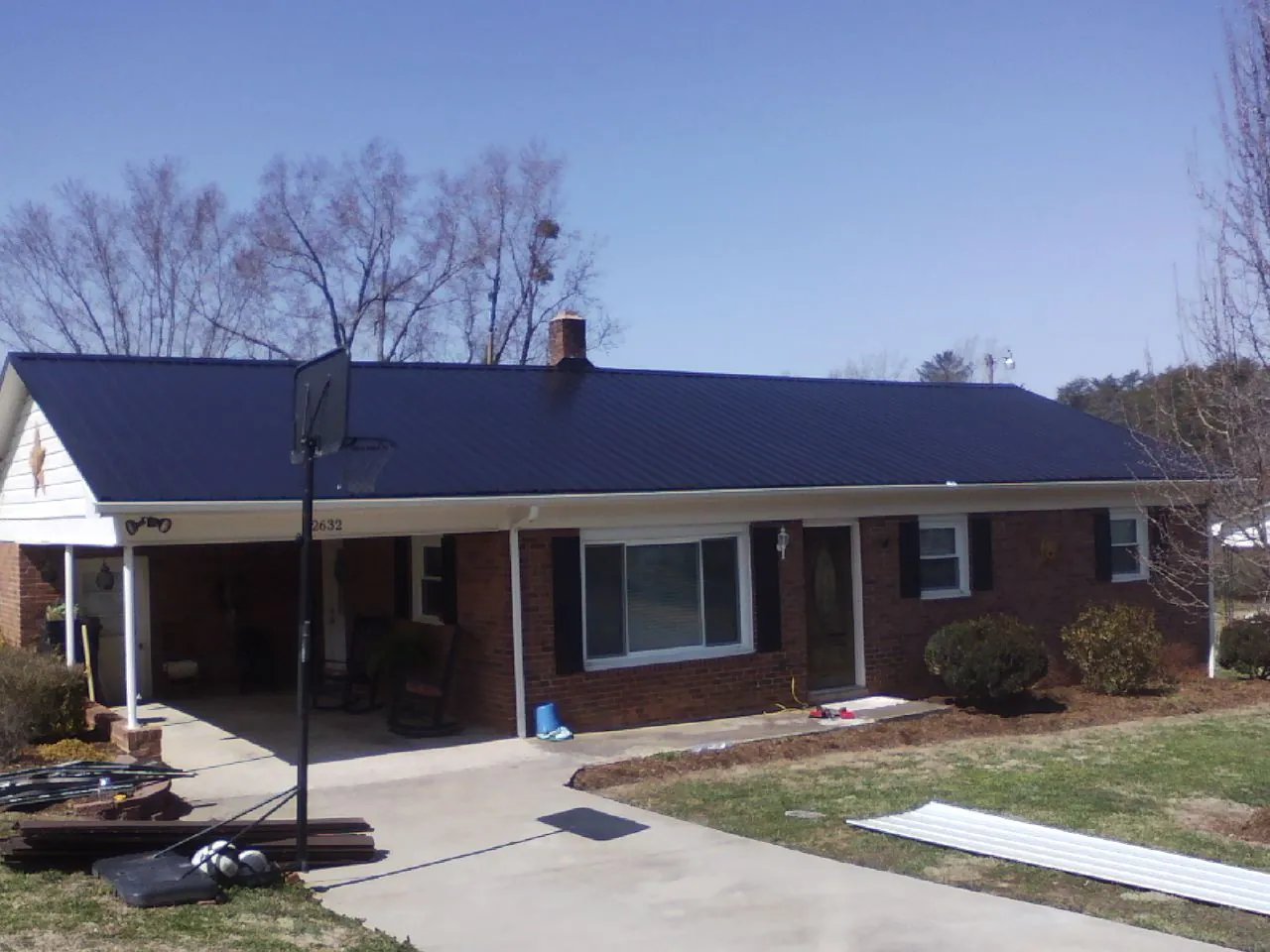 Finished dark blue metal roof on a brick ranch with a carport in Shawboro