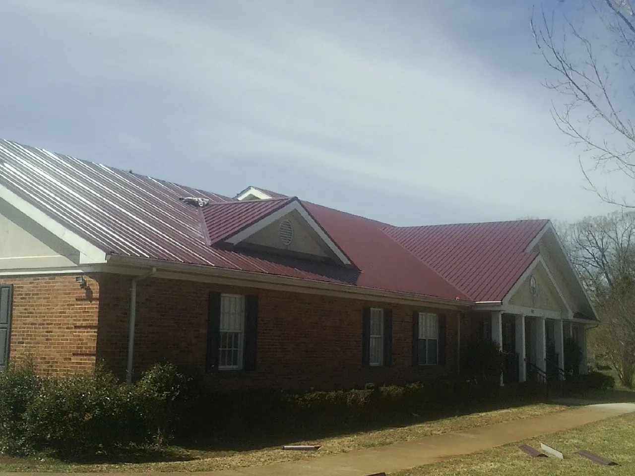 Red metal roof with gabled entries on a long brick building, from a Hail Damage Roof Repair job in Shawboro