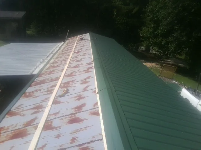 Old rusted panels beside newly installed green metal roofing — Wind Damage Roof Repair by Roofing Brothers in Shawboro