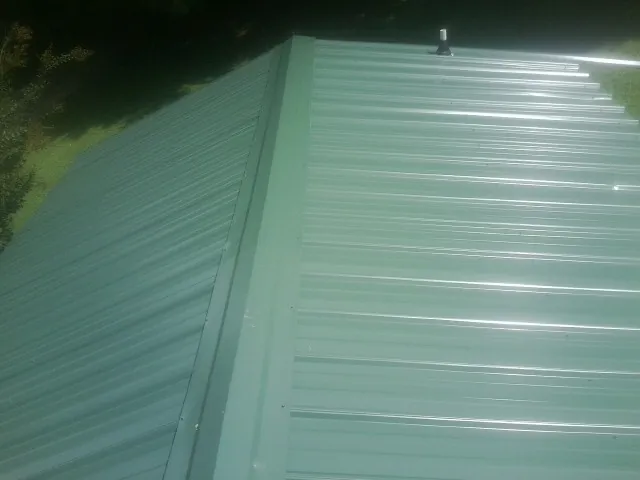 New green metal panels meeting at the ridge of a roof — Flat Roof Repair work by our crew in Shawboro
