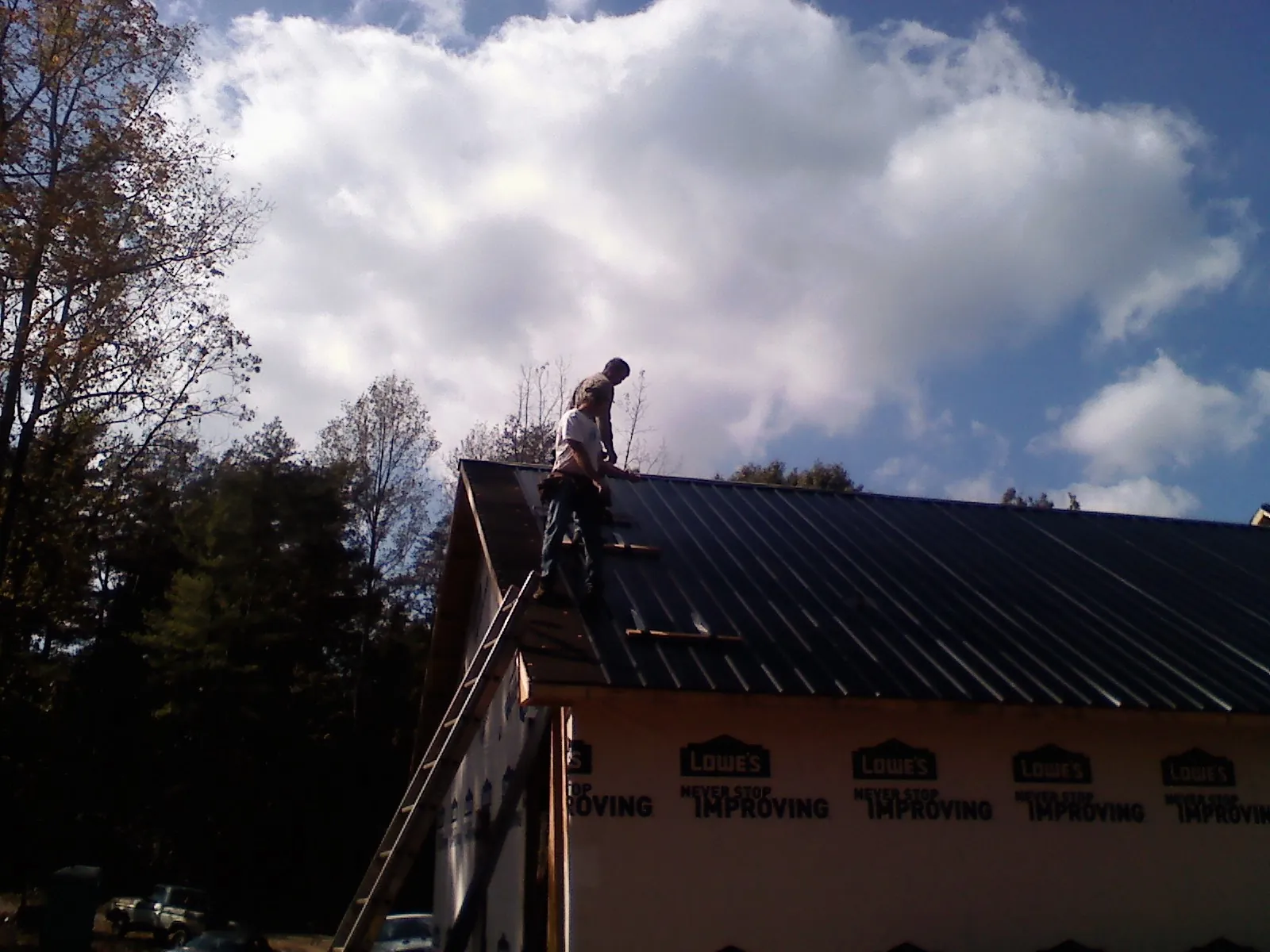 Roofer fastening dark metal panels high against a cloudy sky, from a Roof Inspection job in Shawboro