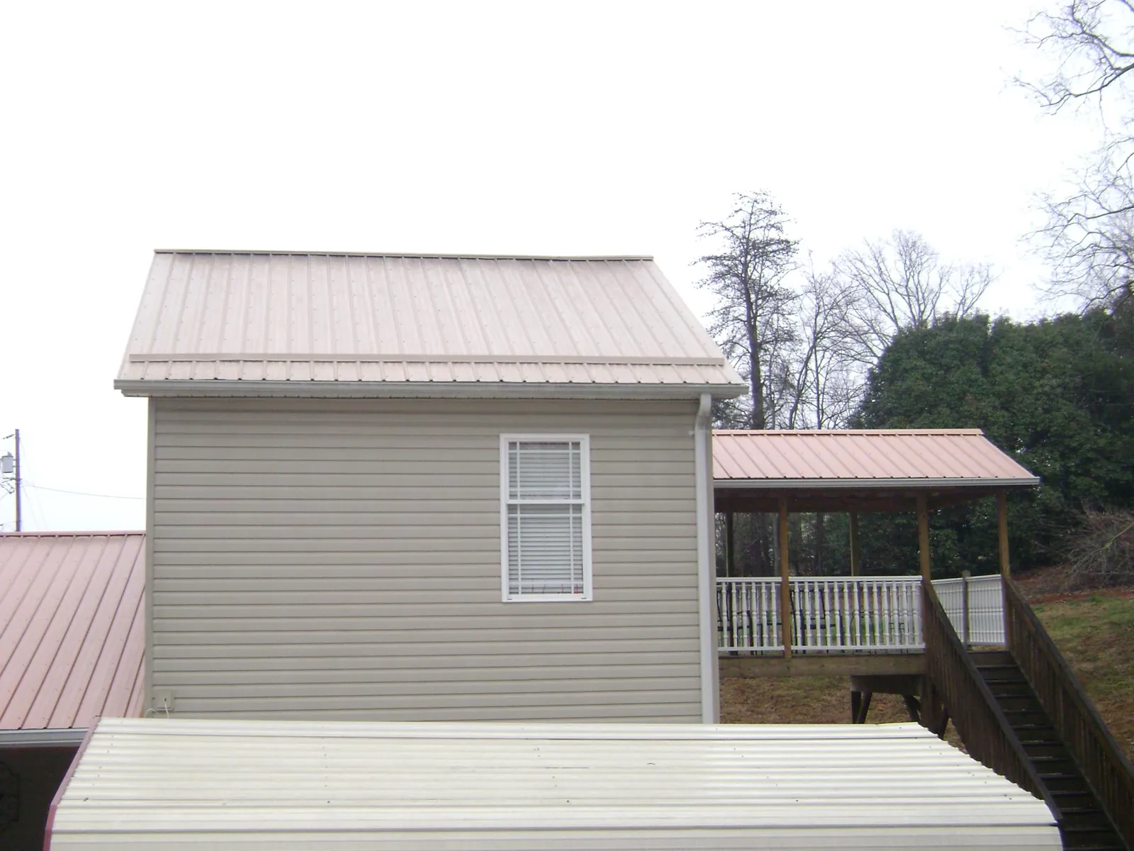 Tan metal roofs on a two story addition and attached porch, from a Roof Replacement job in Shawboro